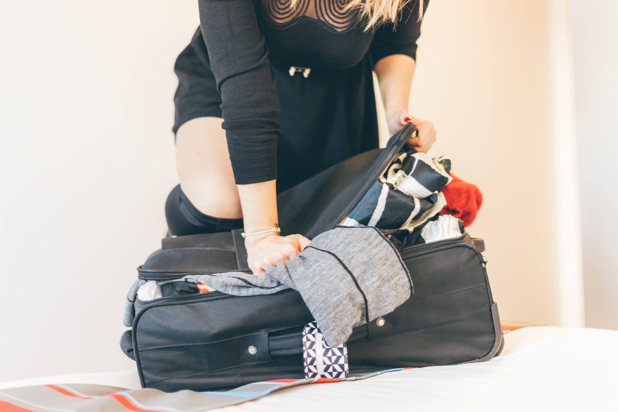 woman shoving clothes in luggage